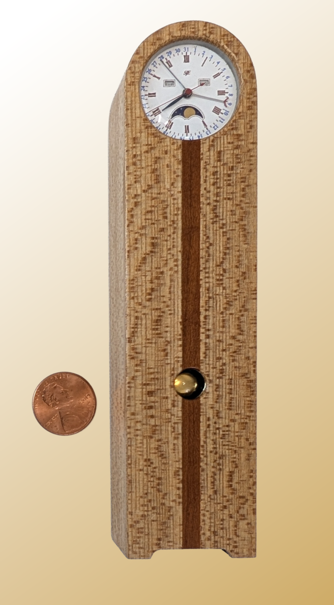 Clock With Calendar and Moon Phase Miniature Clock with Calendar and Moon Phase. Materials: Quarter sawn sycamore with cherry accent strip, steam bent and lacquered. Plastic inner frame, movement, and battery holder (PLA). Glass dial cover and bob window. 1.3x5.5x.9